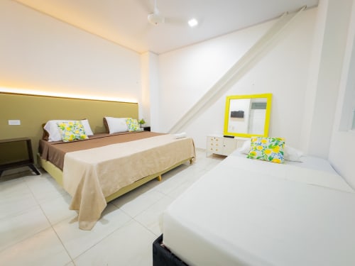 Habitación triple del hotel La Puerta del Angel en Ricaurte con dos camas, espejo amarillo, almohadas coloridas y comodidades modernas
