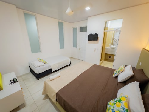 Habitación triple del hotel La Puerta del Ángel en Ricaurte con dos camas, televisor y baño privado