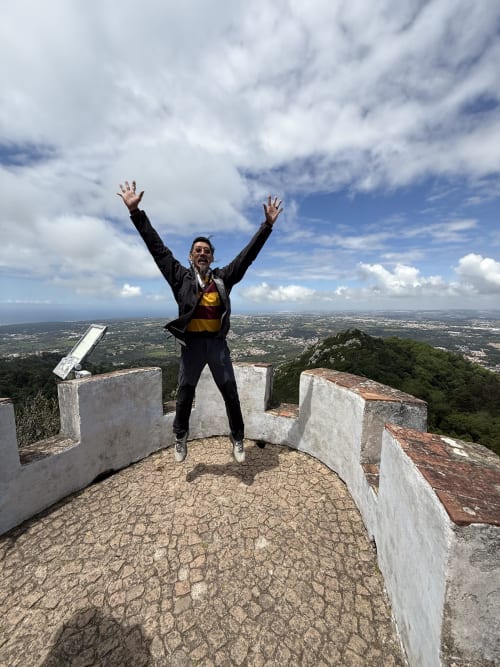 Homem saltando com os braços erguidos nas ruínas de montanha com vista para a paisagem de Ribeirinha, Portugal