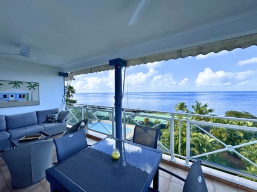 Beachfront terrace at Horizon Doré in Gourbeyre with ocean views, lounge seating, and palm trees