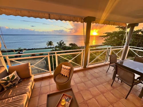 Sunset terrace at Horizon Doré with ocean view, lounge seating, and palm trees in Gourbeyre