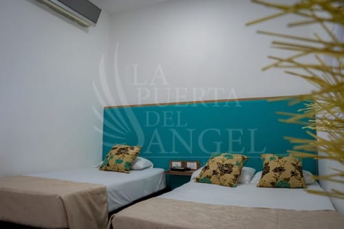 Habitación de hotel con dos camas, almohadas florales y cabecera turquesa en La Puerta del Angel, Ricaurte