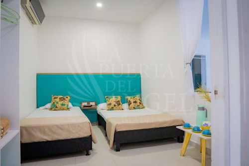 Habitación luminosa en La Puerta del Angel con dos camas, almohadas amarillas estampadas, cabecero turquesa y mobiliario moderno