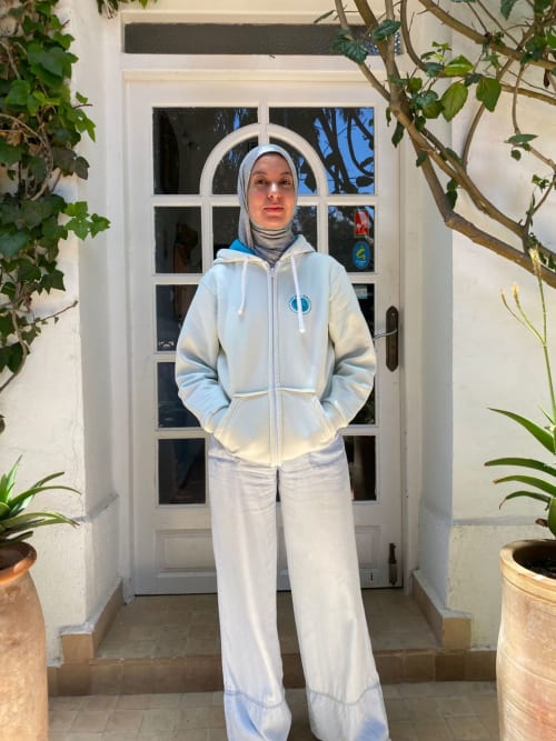 Guest in light blue hoodie and white pants at Vent Des Dunes & Spa entrance in Essaouira, Morocco