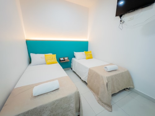 Camas gemelas en la Habitación 207 del hotel La Puerta del Ángel en Ricaurte con cabecero turquesa y almohadas amarillas