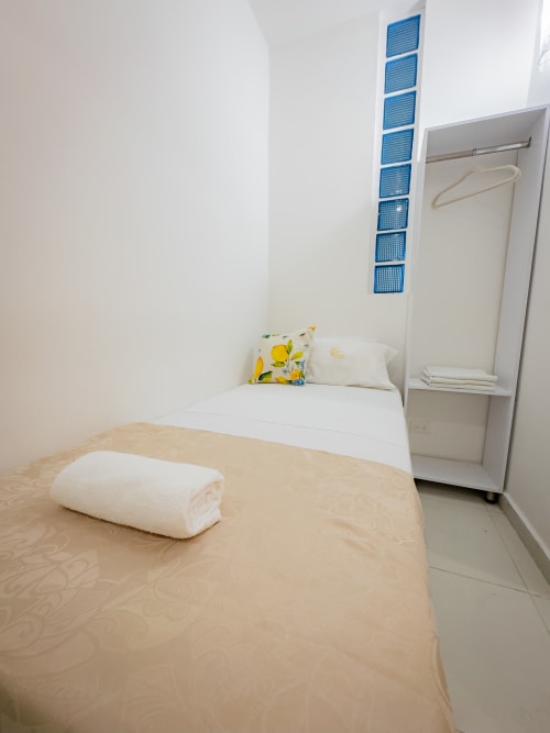 Habitación luminosa en hotel La Puerta del Angel, Ricaurte con camas gemelas, almohadas blancas, toalla enrollada, armario y azul