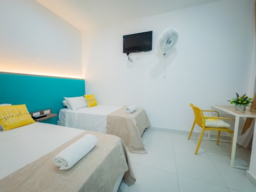 Habitación moderna en La Puerta del Angel con camas gemelas, cabecero turquesa, almohadas amarillas, TV, ventilador y escritorio