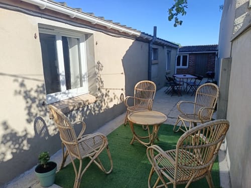 Sunny courtyard patio at Maison Le Wetz with rattan chairs, round table, and artificial grass, surrounded by modern apartment