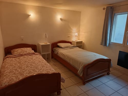 Twin bedroom at Les Meublés d'Hélène with wooden beds, bedside tables, wall sconces, and window in Sainte-Marie-Kerque