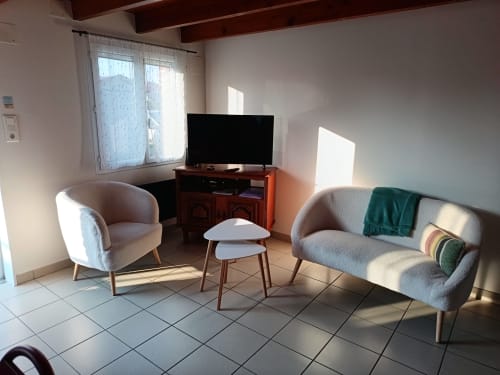 Bright living room at Les Meublés d'Hélène with grey armchairs, wooden TV stand, and white side table in Sainte-Marie-Kerque
