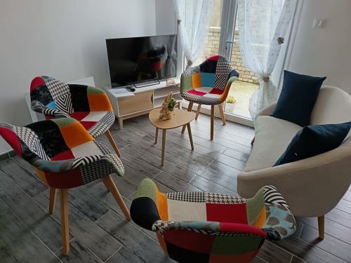 Modern living room at Les Meublés d'Hélène with colorful patchwork chairs, wooden table, flat-screen TV, and glass doors