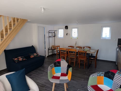 Modern open-plan living room with dining area at Les Meublés d'Hélène apartment. Features navy sofa, colorful accent chairs,