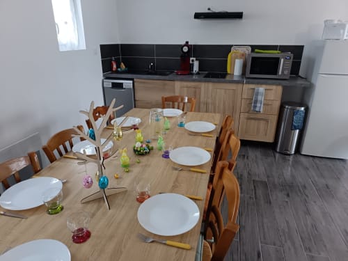 Dining area in Maison La Tour Penchée apartment with wooden table set for guests, modern kitchen with appliances visible in