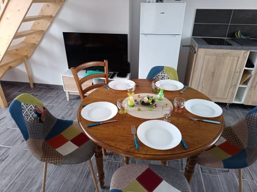 Salle à manger de l'appartement Maison Le Platier d'Oye avec table ronde en bois dressée pour cinq, chaises colorées et cuisine ouverte