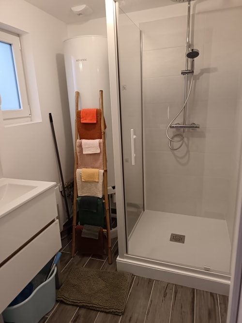 Salle de bain moderne aux Meublés d'Hélène avec douche à l'italienne, carrelage blanc, échelle porte-serviettes en bois et chauffe-eau Atlantic.