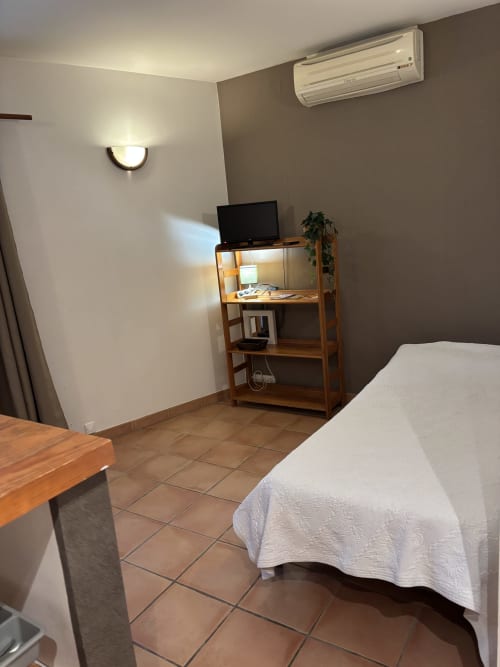 Chambre de l'appartement Eglantine à Anne De La Maison Blanche, Avignon avec lit, étagères en bois, TV, climatisation et applique murale