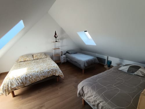 Bright attic bedroom at Les Meublés d'Hélène with three beds, skylights, wooden floors, and minimalist decor