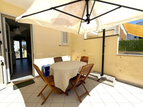 Terrazza esterna per dining presso l'appartamento Villetta Alba di Puglia Estate con tavolo rotondo, sedie in legno e ombrelloni color crema