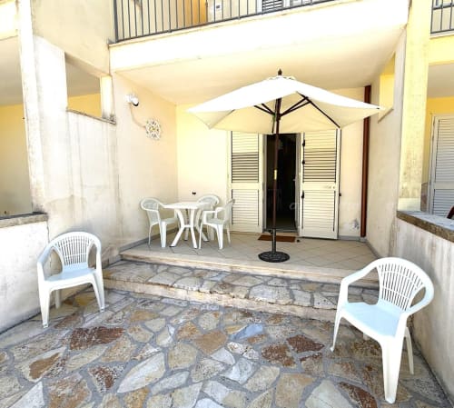 Cortile giardino di Puglia Estate Villetta Alba con sedie bianche, ombrellone e terrazza in pietra a Nardò, Italia