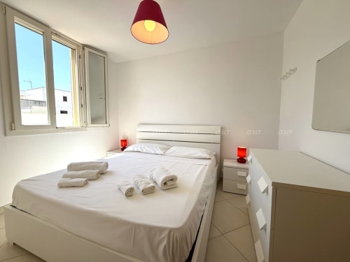 Camera luminosa della Villetta Alba con letto bianco, lampada rossa e vista sui giardini di Nardò