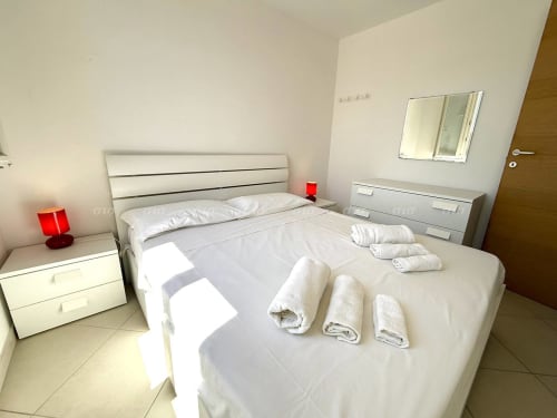 Camera moderna della Villetta Alba a Puglia con letto bianco, asciugamani arrotolati, lampade rosse e specchio a Nardò, Italia