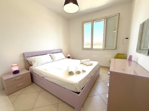 Luminosa camera da letto nella Villetta Alba di Puglia Estate con letto viola, biancheria bianca, asciugamani arrotolati, comodino e finestre