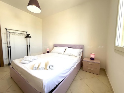 Camera da letto moderna a Puglia Estate con letto viola, biancheria bianca, comodino e lampada a soffitto