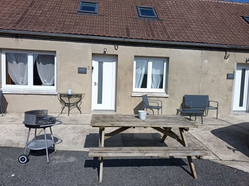 Terrasse extérieure de l'appartement Les Escardines avec table de pique-nique en bois, barbecue, chaises longues et façade en pierre beige