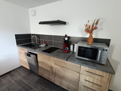 Cuisine moderne aux plans de travail noirs, armoires en bois, évier, cuisinière, micro-ondes et fleurs décoratives aux Escardines
