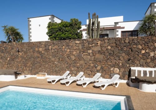 Villa Estrella Polar's pool area in Tahiche with loungers, volcanic stone wall, and white modern architecture under clear