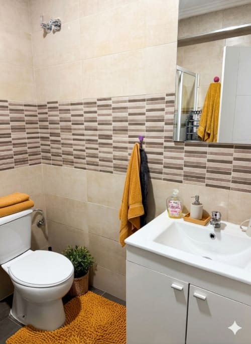 Baño moderno en el apartamento Torre Sol Y Playa en Torremolinos con azulejo a rayas, lavabo blanco, inodoro y accesorios dorados