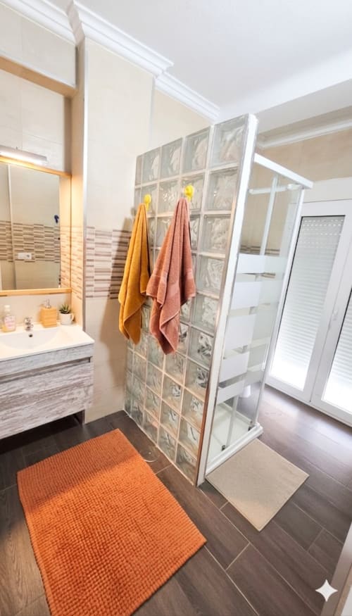 Moderno cuarto de baño del apartamento Torre Sol Y Playa en Torremolinos con ducha de cristal, lavamanos y alfombra de baño naranja