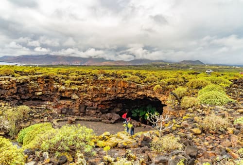 Lava cave with verdant vegetation and hikers in Lanzarote's volcanic landscape near Tahiche