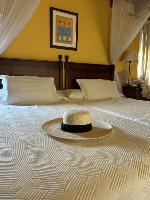 L'Albureca room at Casa Gallinera boutique vacation home in Alicante with yellow walls, dark wood bed, and straw hat on bed