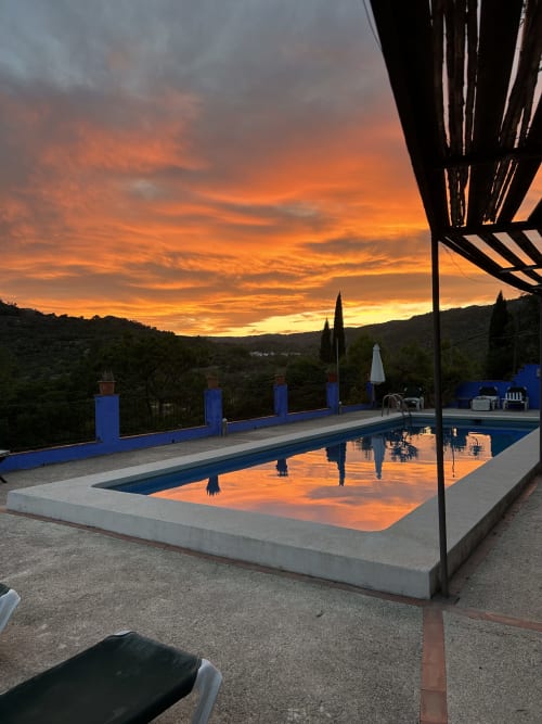 Sunset reflecting in Casa Gallinera's pool with blue-rimmed terrace, cypress trees, and Alicante hills at dusk