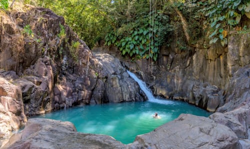 Turquoise waterfall pool in rocky canyon gorge with swimming guest near Le Gosier