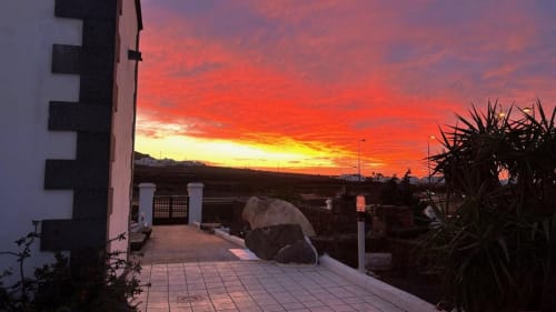 Stunning sunset view from Villa Estrella Polar terrace in Tahiche, with vibrant orange and red skies over the garden