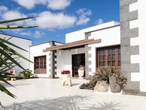 Villa Estrella Polar terrace in Tahiche with white walls, wooden doors, potted flowers, and mountain views under blue sky
