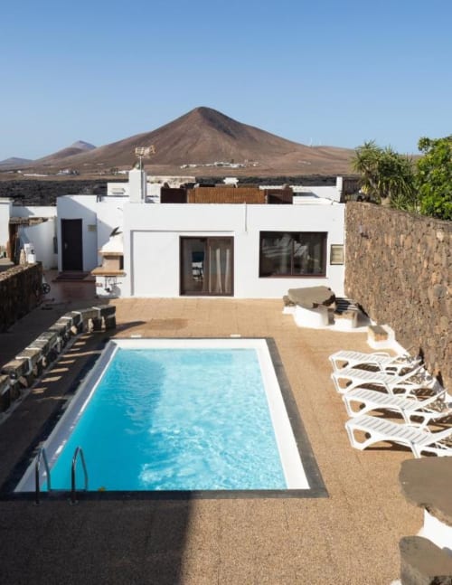 Modern white villa with swimming pool and mountain view in Tahiche, Lanzarote, featuring lounge chairs and terrace