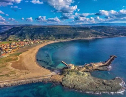 Vista aerea della spiaggia sabbiosa di Bosa, baia turchese, relitto sommerso e villaggio arroccato in Sardegna