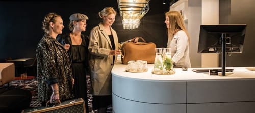 Quattro donne alla reception di Regnos Altos Boutique Rooms, elegante hall del hotel Bosa con arredi raffinati