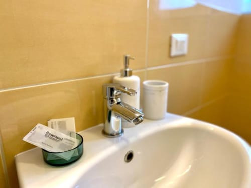 Clean bathroom sink with chrome faucet, soap dispenser, and amenities at The Green Gate guest house in Pisa