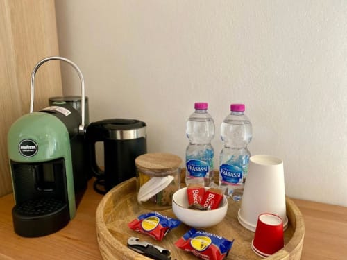 Amenità di benvenuto su vassoio in legno: macchina caffè Lavazza verde, bottiglie d'acqua, snack e articoli da toilette in camera doppia