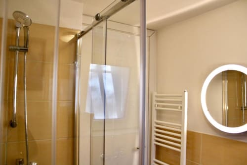 Modern bathroom at The Green Gate with glass shower enclosure, illuminated round mirror, and heated towel rack in Pisa hotel