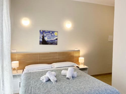 Camera da letto moderna e spaziosa presso The Green Gate Guest House a Pisa con testata in legno, asciugamani arrotolati, opere d'arte e atmosfera accogliente
