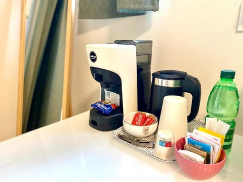 Hotel room beverage station with coffee maker, kettle, green bottle, and hospitality amenities at The Green Gate Airport