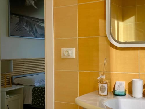 Bagno con piastrelle gialle, lavabo bianco, specchio e accessori da bagno presso la guest house The Green Gate a Pisa