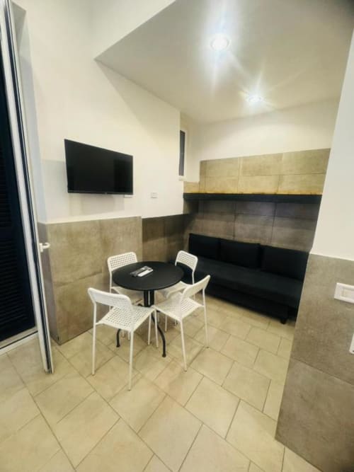 Modern apartment dining area with black round table, white chairs, beige tile flooring, and wall-mounted TV at Neapolis