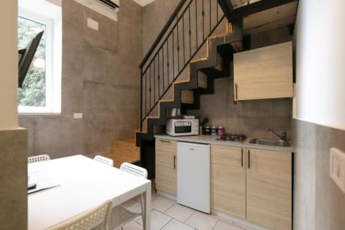 Modern kitchen and dining area in Two-Bedroom Apartment with black staircase, wood cabinets, and tile flooring at Neapolis