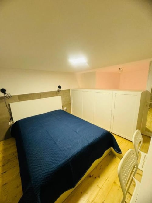 Bedroom with blue bedspread, white headboard, wooden floors, cream walls, and white storage cabinets at Neapolis Tecnotourist